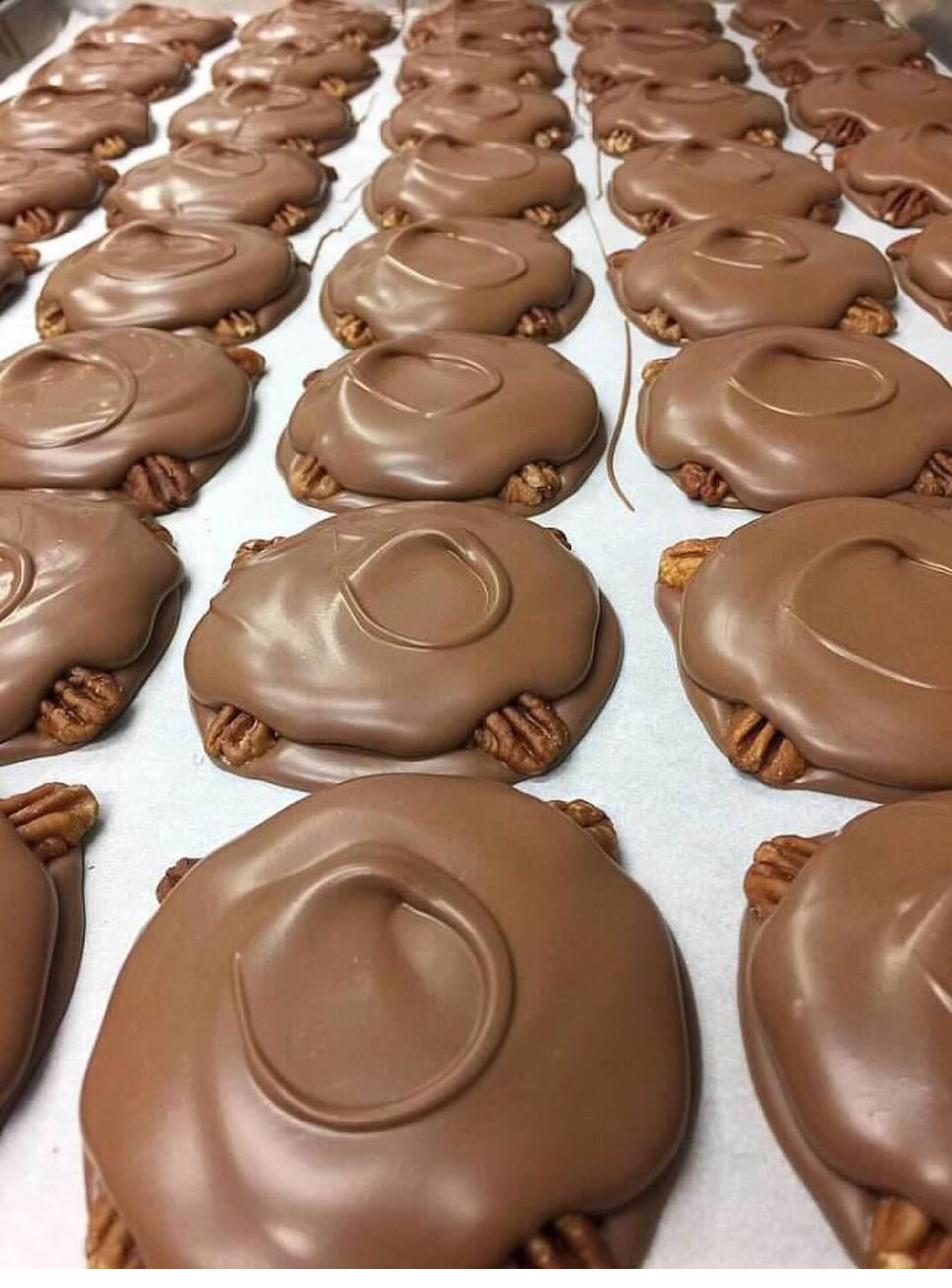 Trays of fresh hand-dipped pecan turtles cooling on parchment paper